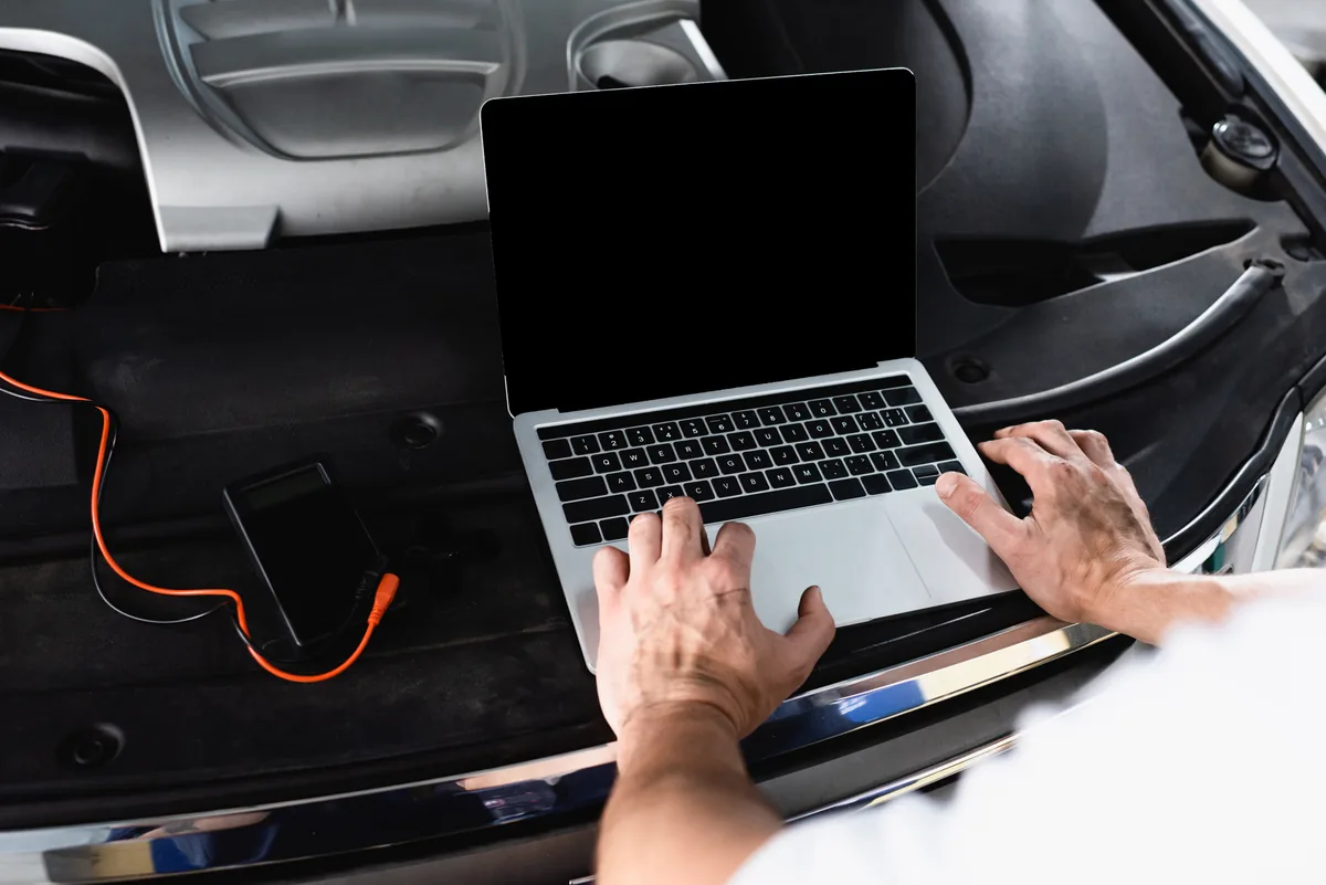 A laptop connected to a car, reading diagnostics from the OBD2 port